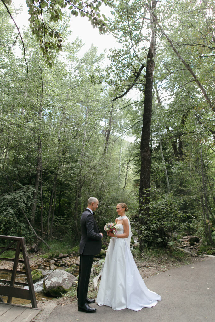A bride and a groom face each other by the bridge near The Chapel at Beaver Creek.