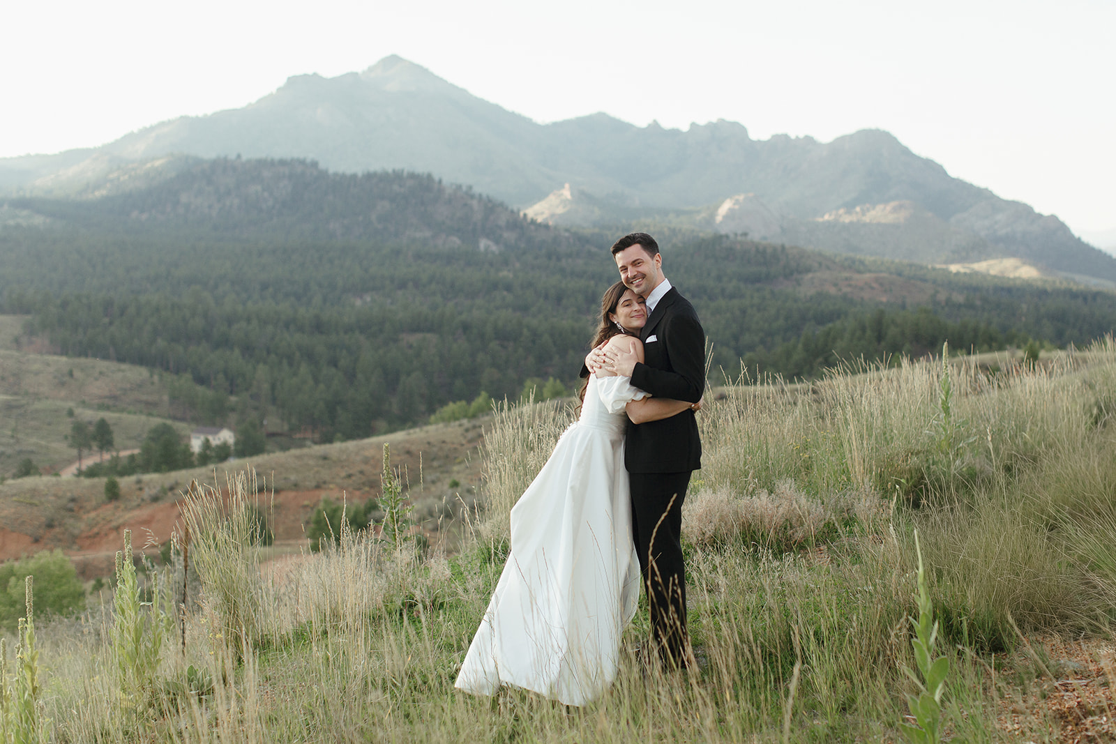 Newlyweds poses at sunset with views of Pikes Peak behind them at Pikes Peak Ranch in Woodland Park, Colorado. Photographed by Jordan Katz.