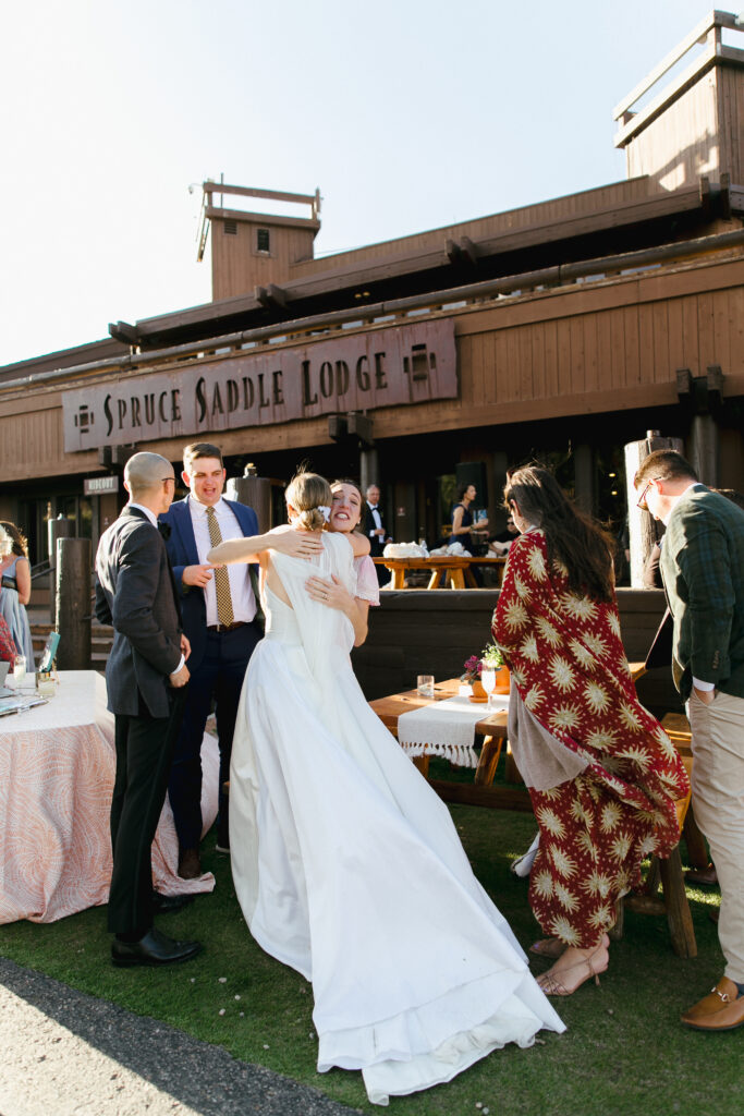 Bride hugs friend at cocktail hour outside Spruce Saddle Lodge at Beaver Creek Resort.